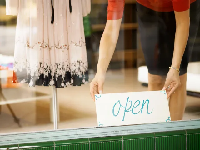 A person holding an open sign in front of a store window.
